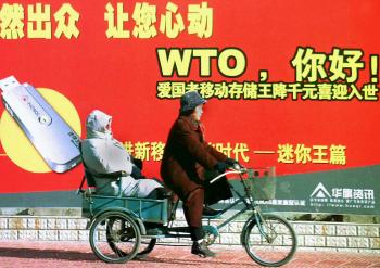 A Chinese couple on a tricycle pass a billboard welcoming the country's membership to the World Trade Organisation (WTO), along a street in Beijing, 23 December 2001. Image credit: AFP/Getty Images