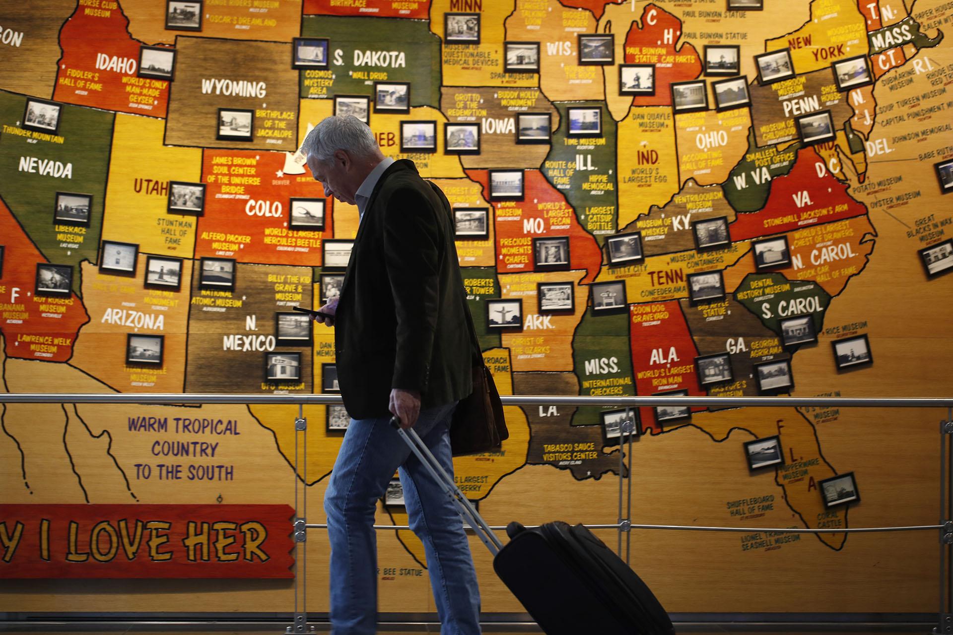 In this March 18, 2020 photo, a traveler checks his mobile telephone while passing a map of the United States on the way to the security checkpoint in the main terminal in Denver International Airport. (AP Photo / David Zalubowski)
