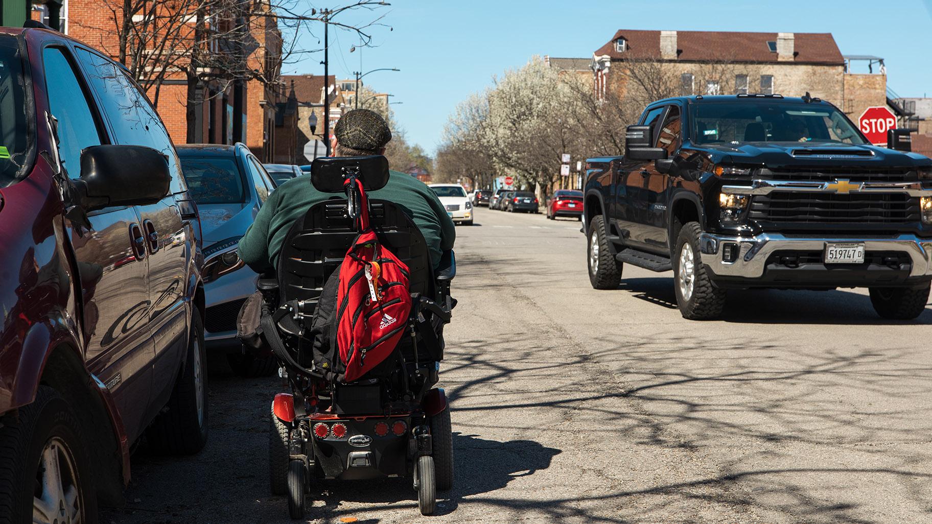 Adam Ballard rides through the street on his electric wheelchair to avoid an inaccessible sidewalk near his Pilsen residence. (Michael Izquierdo / WTTW News)
