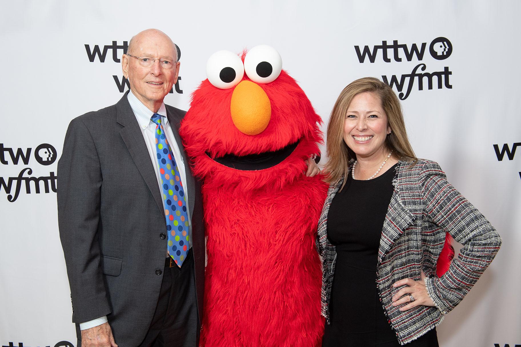 Jim Mabie and Sandra Cordova Micek, president and CEO of WTTW and WFMT, pose with Elmo from “Sesame Street.” (WTTW)