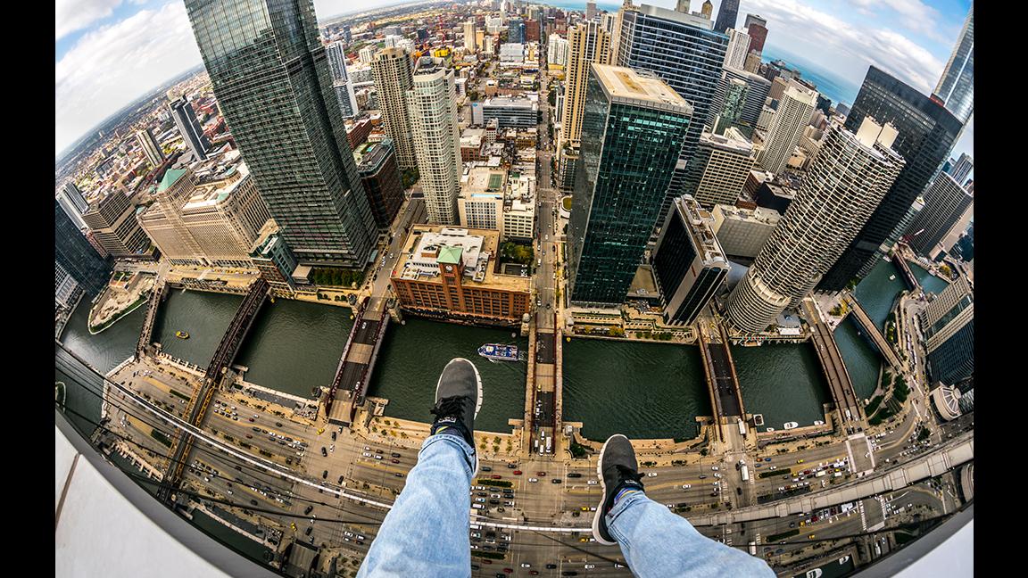 A self-described “rooftopper” dangles his feet, a familiar perspective for such photographers, while sitting atop a Chicago skyscraper. (Courtesy Andrew Fitzsimmons)