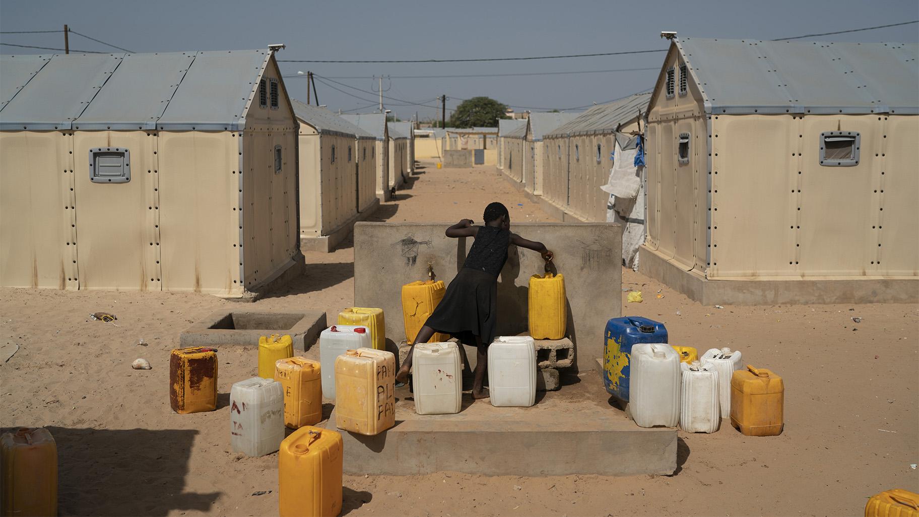 A young girl fills water containers at a camp for internally displaced people who lost their coastal homes to erosion from the Atlantic Ocean in Saint Louis, Senegal, Thursday, Nov. 4, 2021. (AP Photo / Leo Correa, File)