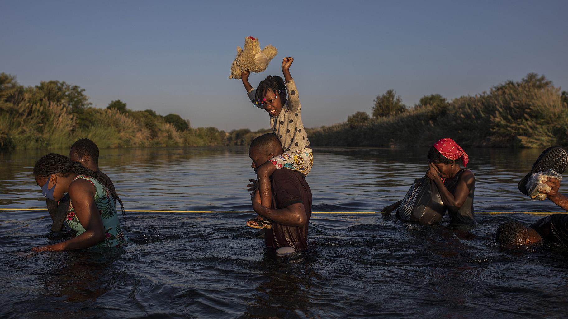 A little girl holds her stuffed animal high above the water as migrants, many from Haiti, wade across the Rio Grande river from Del Rio, Texas, to return to Ciudad Acuña, Mexico, Monday, Sept. 20, 2021, to avoid deportation. (AP Photo / Felix Marquez)