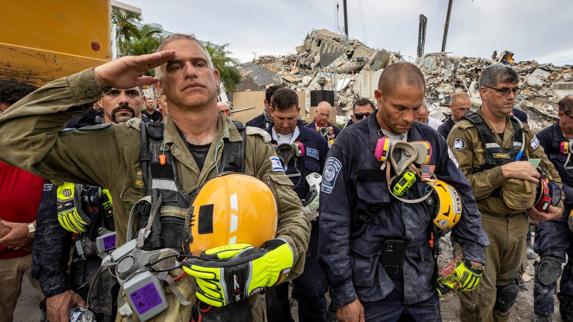 A member of the Israeli search and rescue team, left, salutes in front of the rubble that once was Champlain Towers South during a prayer ceremony, Wednesday, July 7, 2021, in Surfside, Fla. (Jose A Iglesias / Miami Herald via AP)
