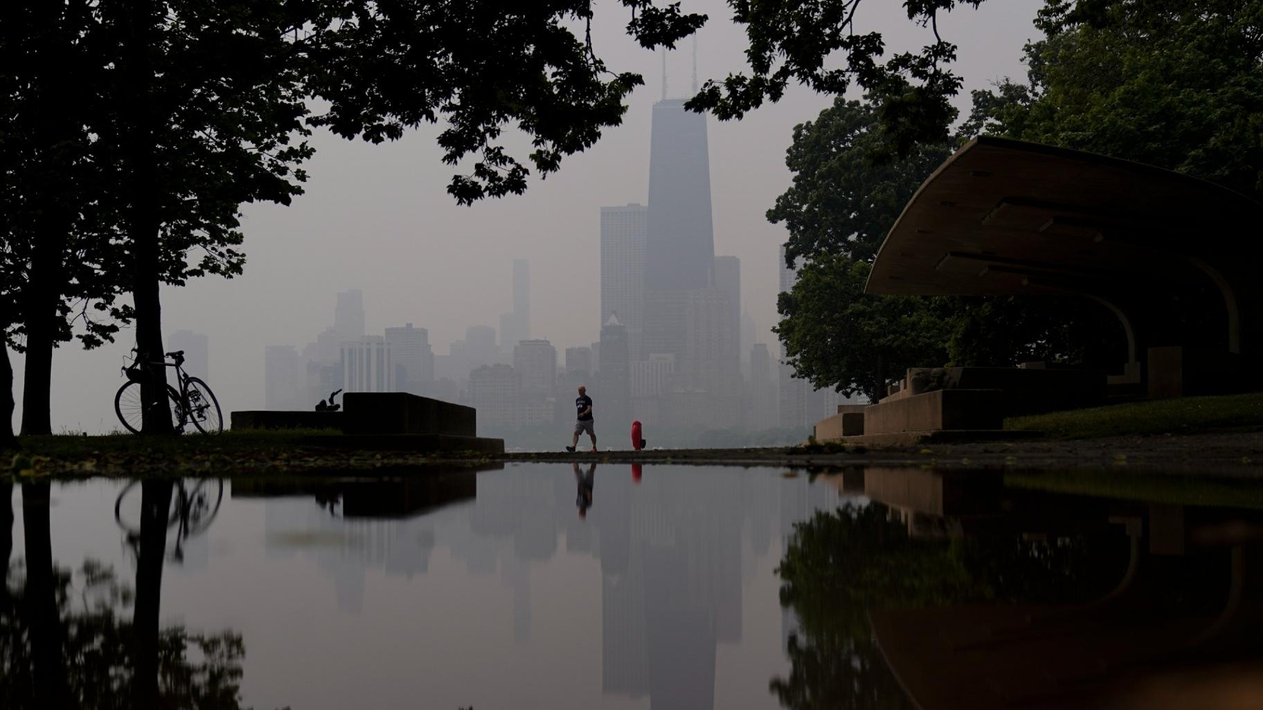 FILE - A person walks along the shore of Lake Michigan as the downtown skyline is blanketed in haze from Canadian wildfires, June 27, 2023, in Chicago. (AP Photo / Kiichiro Sato, File)