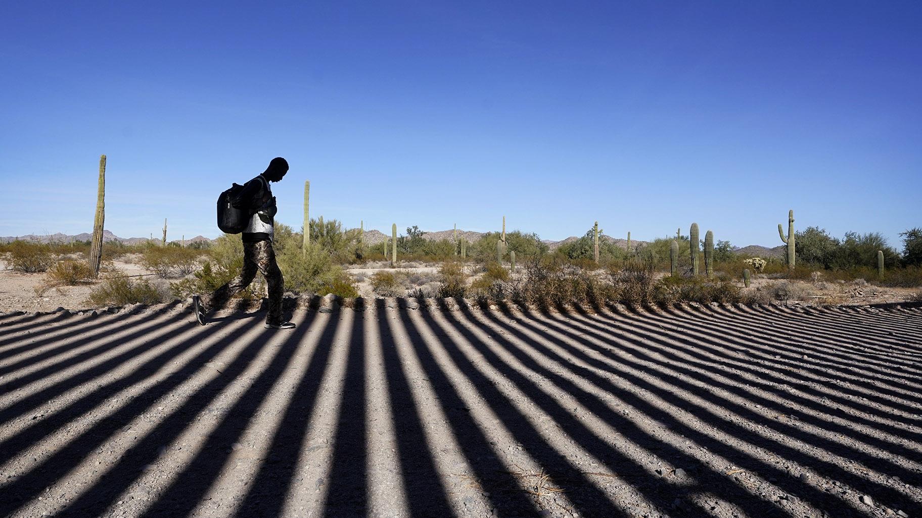 A migrant walks along a road shadowed by the steel columns of the border wall separating Arizona and Mexico after crossing into the United States, Friday, Dec. 15, 2023, near Lukeville, Ariz. (AP Photo / Gregory Bull, File)