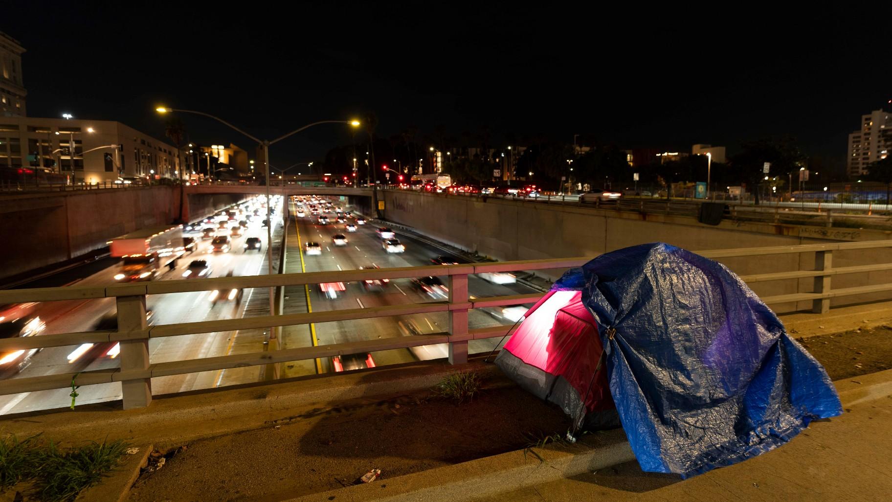 In this photo illuminated by an off-camera flash, a tarp covers a portion of a homeless person's tent on a bridge overlooking the 101 Freeway in Los Angeles, Thursday, Feb. 2, 2023. (AP Photo / Jae C. Hong, File)
