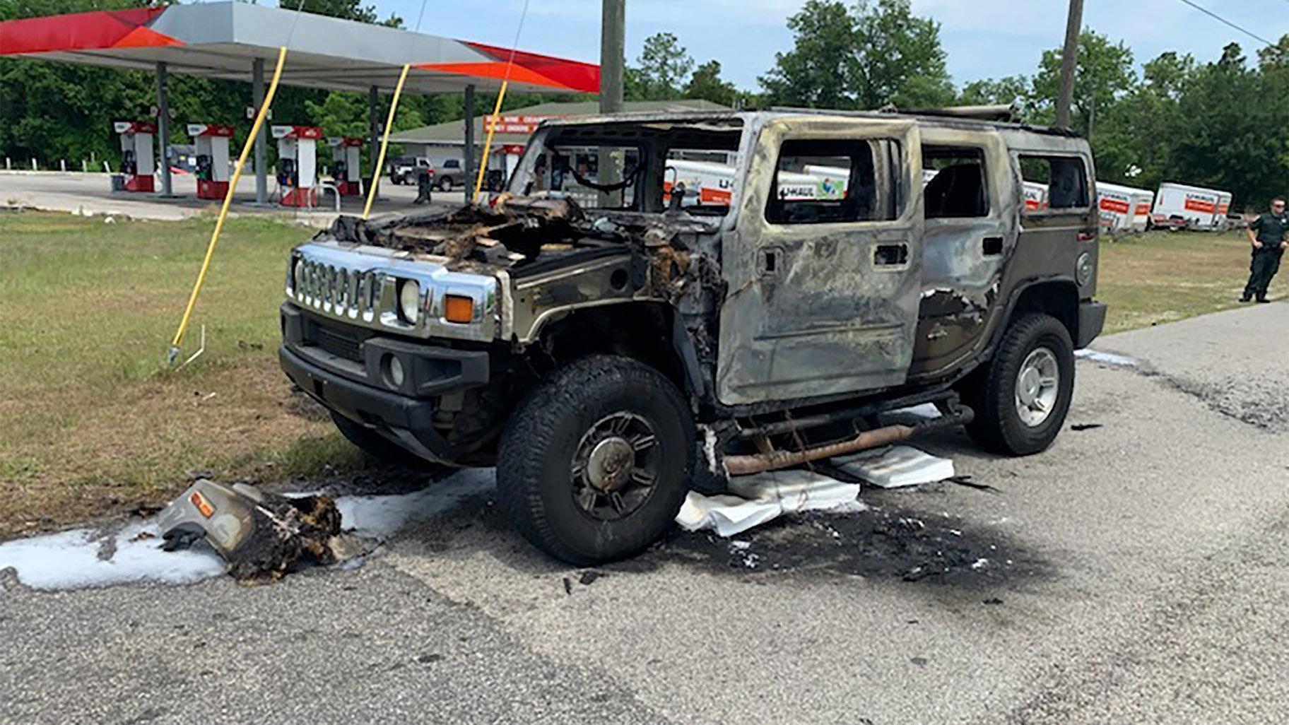 In this photo provided by Citrus County Fire Rescue an officer stands near a Hummer which was destroyed by fire shortly after the driver had filled up four 5-gallon (18-liter) gas containers on Wednesday, May 12, 2021, in Homosassa, Fla. (Citrus County Fire Rescue via AP) 