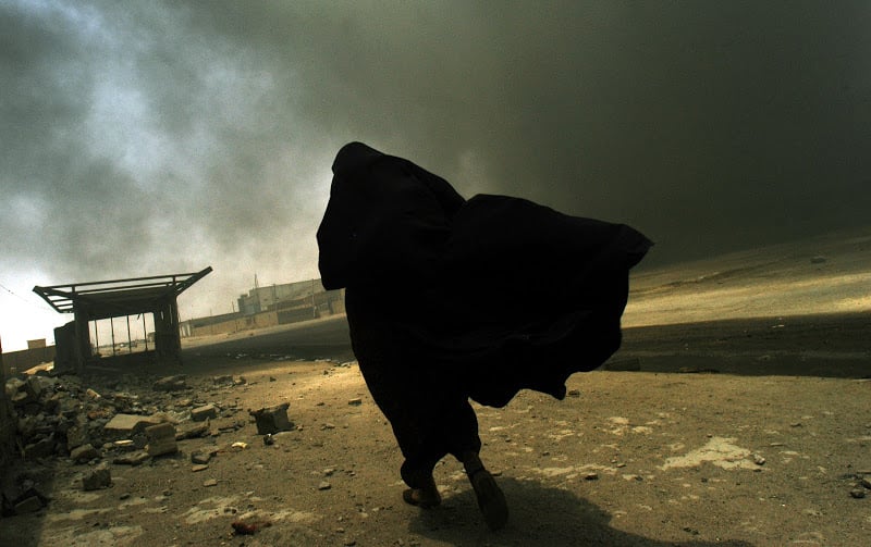 An Iraqi woman walks through a plume of smoke rising from a massive fire as she searches for her husband in Basra, Iraq, May 26, 2003. (Lynsey Addario / Corbis Saba)