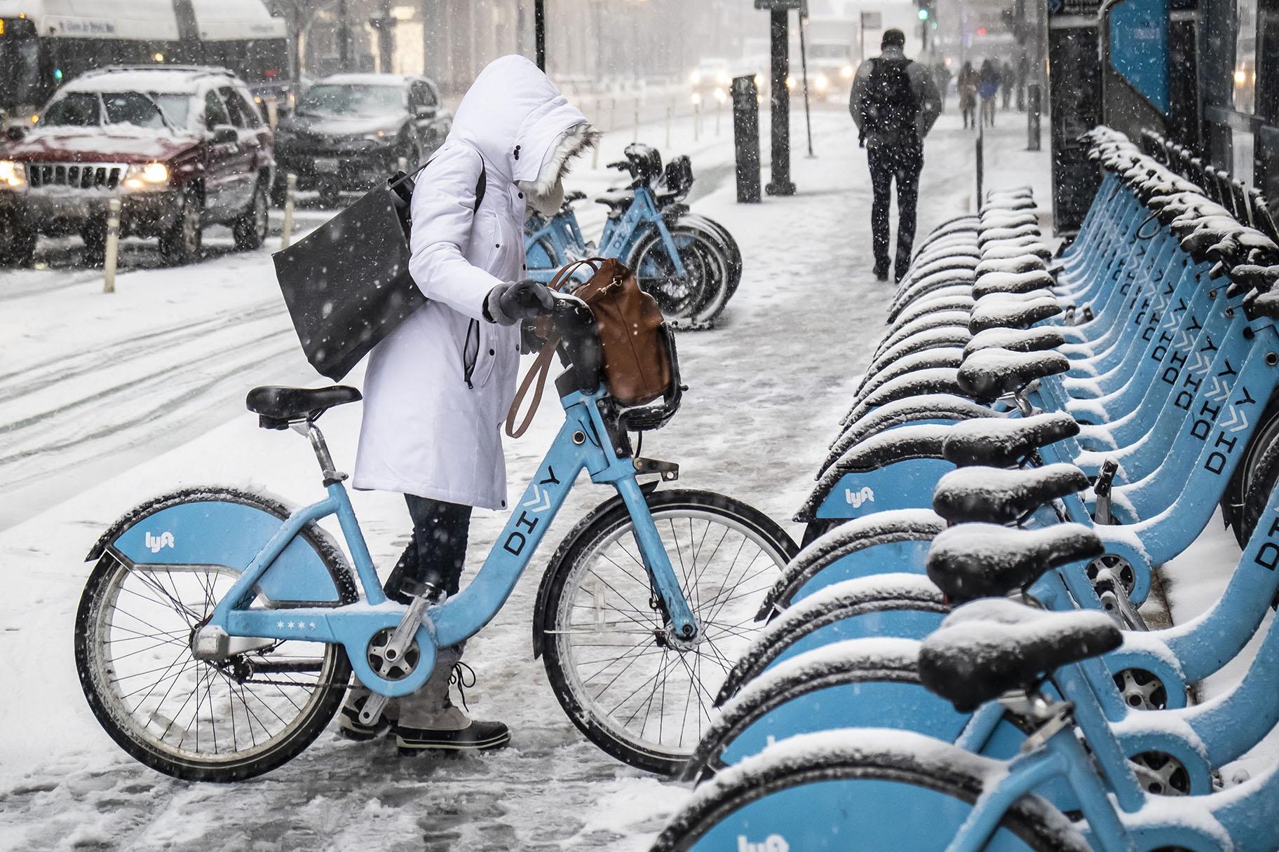 A woman clears off a Divvy bike as a winter weather advisory is issued for the Chicago area on Monday, Nov. 11, 2019, in Chicago. (Rich Hein / Chicago Sun-Times via AP)