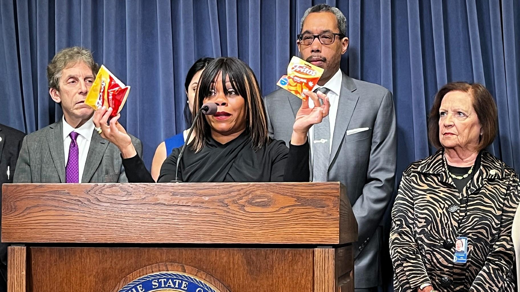 Cannabis Business Association of Illinois Executive Director Tiffany Ingram holds up a bag of Fritos corn chips and a similar-looking bag of “Fritos” snacks with small cannabis leaves on it. CBAI is urging for the state to prohibit sales of delta-8 THC products like the imposter “Fritos.” (Hannah Meisel / Capitol News Illinois)