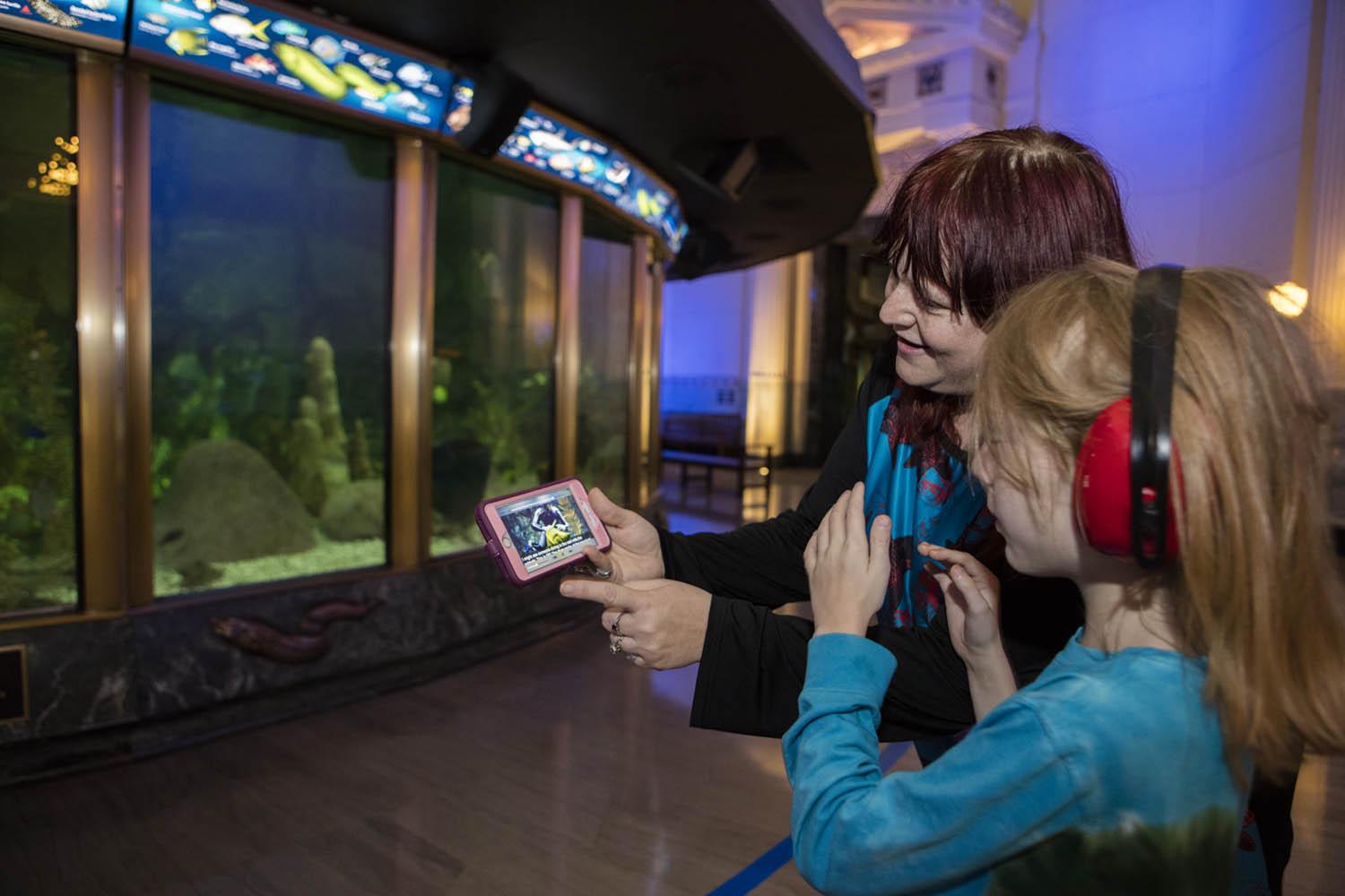 A mother and daughter explore Shedd’s Sensory-Friendly App, designed for guests with autism or a sensory processing disorder, in front of the aquarium’s Caribbean Reef exhibit. (Brenna Hernandez / Shedd Aquarium)