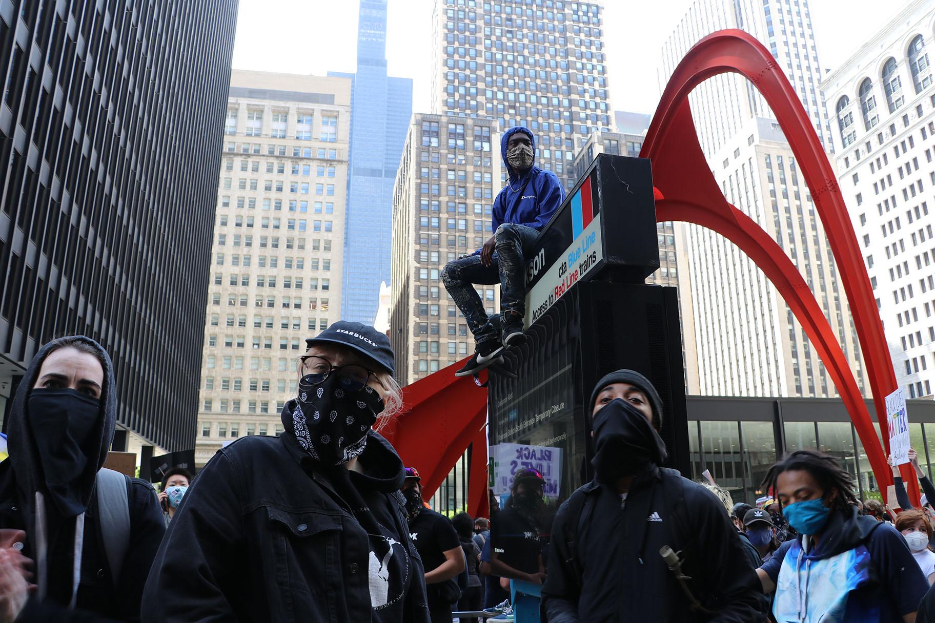 A protester sits on a CTA sign in front of Federal Plaza. (Evan Garcia / WTTW News)