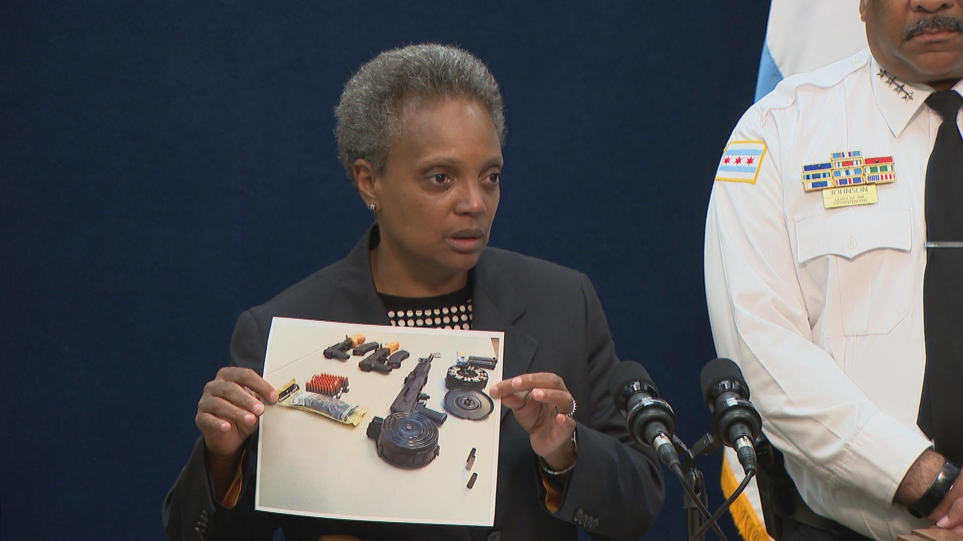 At a press conference Tuesday, Aug. 6, Mayor Lori Lightfoot holds a photograph of evidence seized from two suspects, including armor-piercing bullets and a gun with a customized “drum magazine that can hold 200-plus bullets.” (WTTW News) 