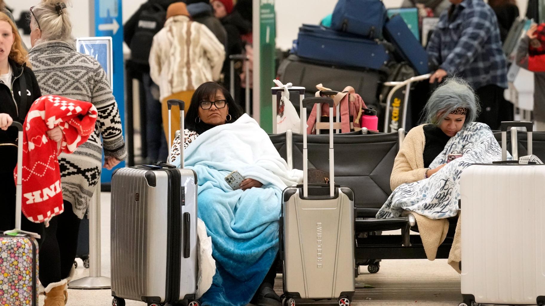 Ana Rosario of Houston, sitting left, tries to keep warm as she waits on her flight in Terminal A at Houston George Bush Intercontinental Airport Tuesday, Jan. 16, 2024, in Houston. (Melissa Phillip / Houston Chronicle via AP)